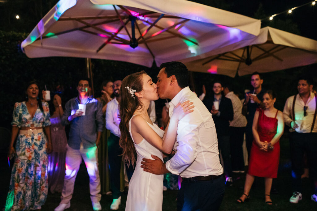 The bride and groom share a romantic kiss amidst the party, capturing the love and connection that continues to blossom on their wedding day