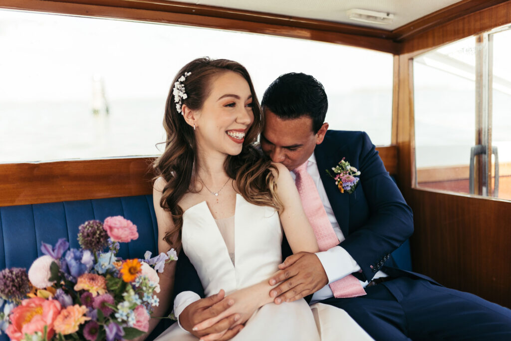 Enchanting portrait of the bride and groom on a water taxi, framed by the picturesque canals of Venice, capturing the romance of their journey to the wedding ceremony