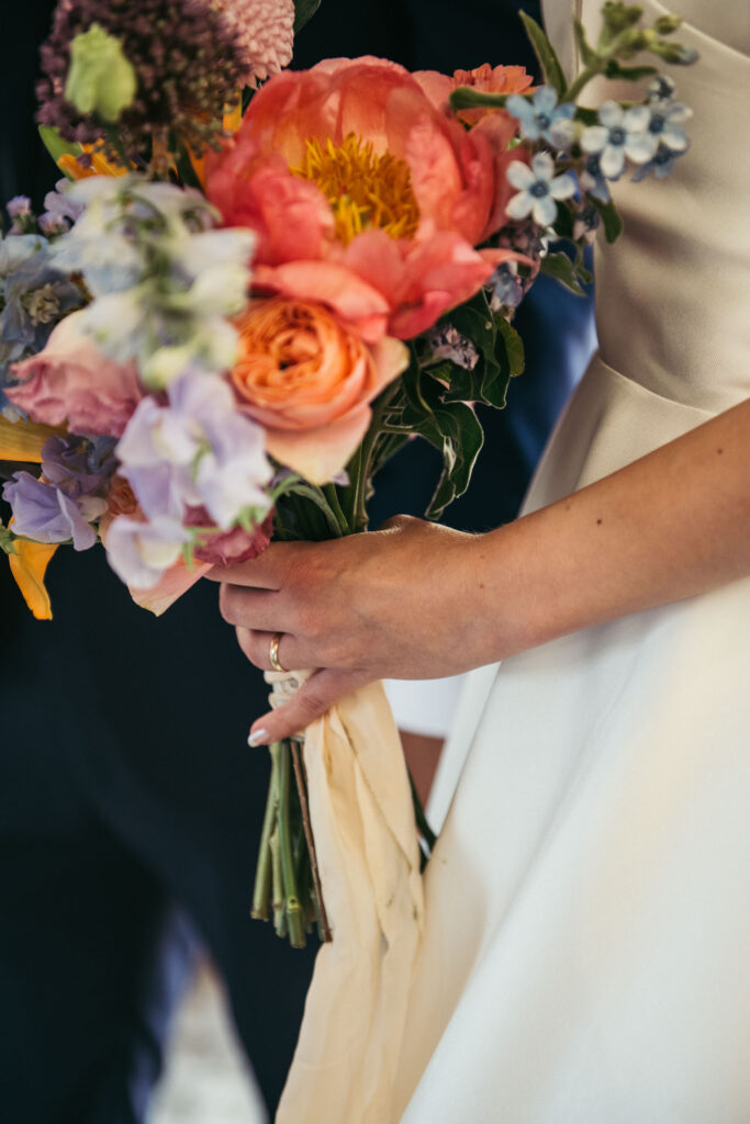 A close-up captures the bride's hand with the wedding band, delicately holding a beautiful bouquet, showcasing the timeless union of love and beauty