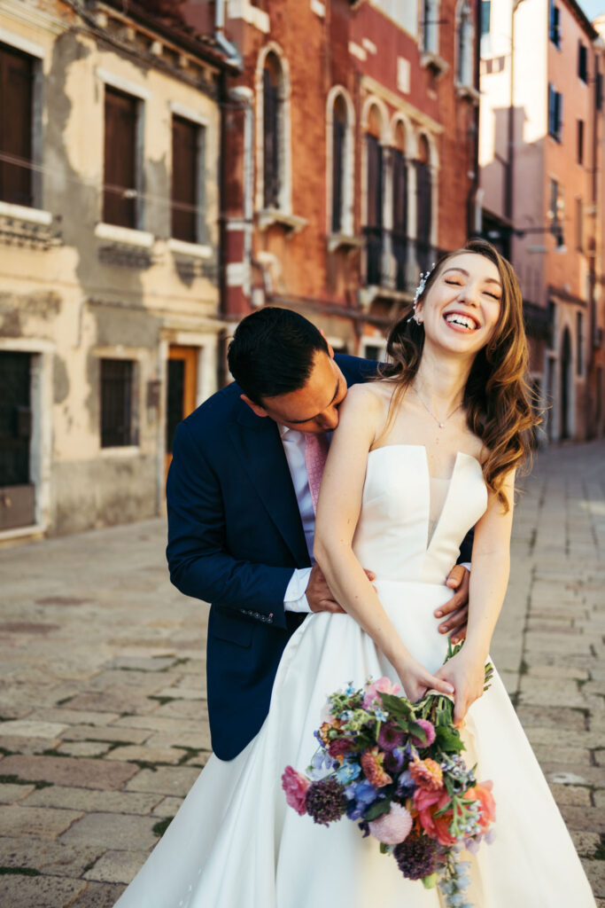 The bride bursts into laughter as the groom tenderly kisses her shoulder during this Venice Intimate Elopement