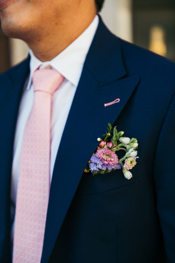 A close-up reveals the charm of pink flowers tucked in the groom's pocket, adding a touch of style to his attire