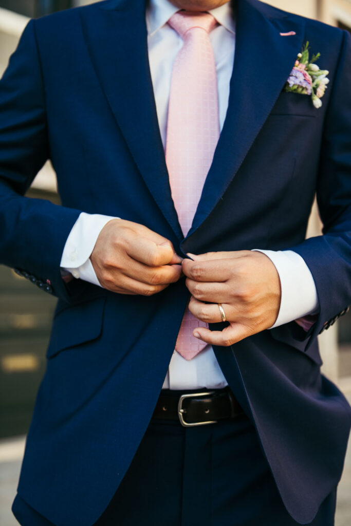 A close-up of the groom's hands buttoning his jacket, showing sophistication and elegance