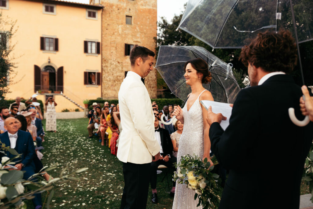 Bride and groom are facing each other during the ceremony, she holds an umbrella because it started to rain