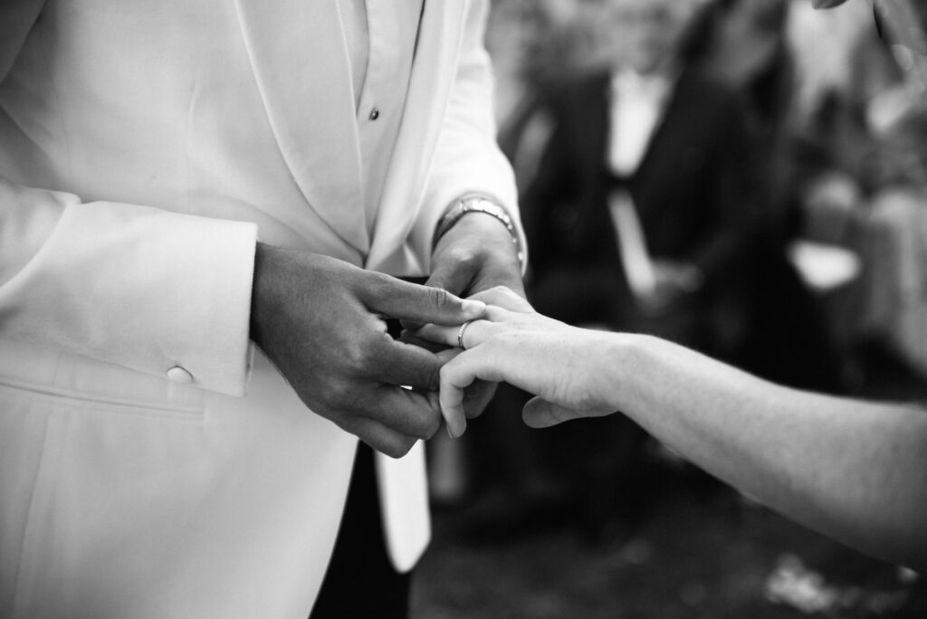 Black and white photo of the groom putting the ring on wife's hand