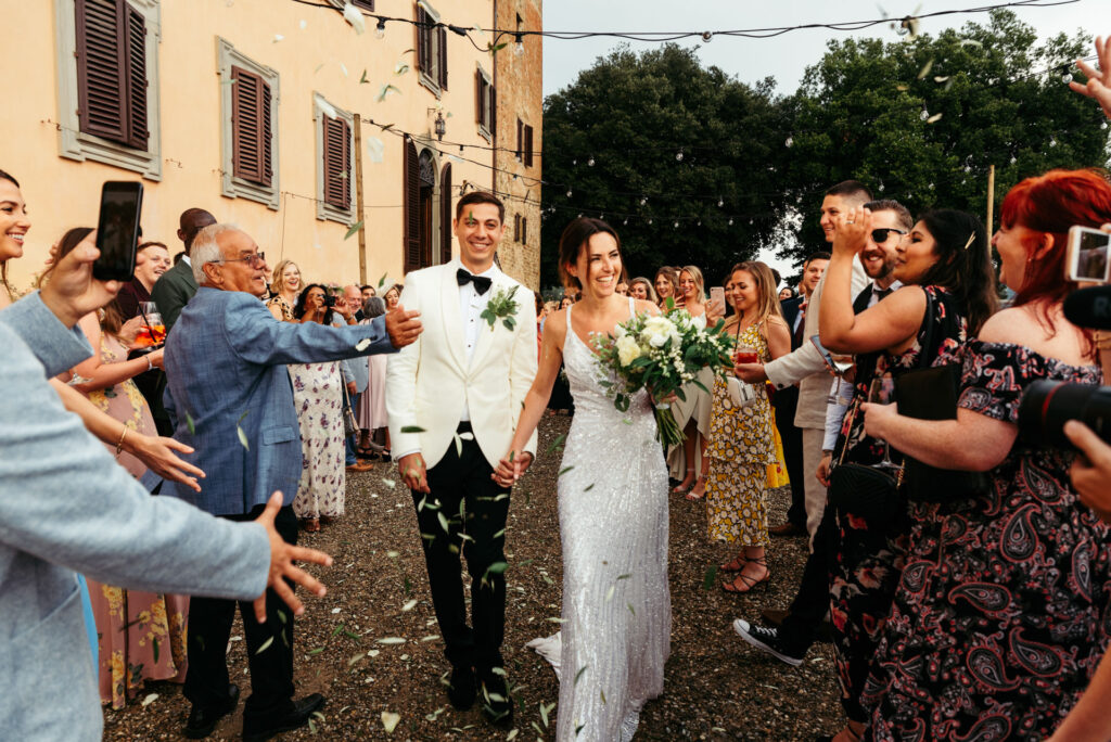 Bride and groom pass between guests throwing confetti and cheering them