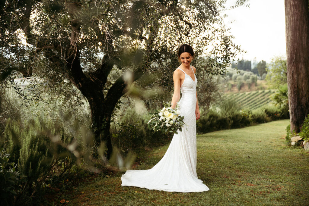 Bride holds her white roses bouquet while posing between olives trees in Tuscany, Italy