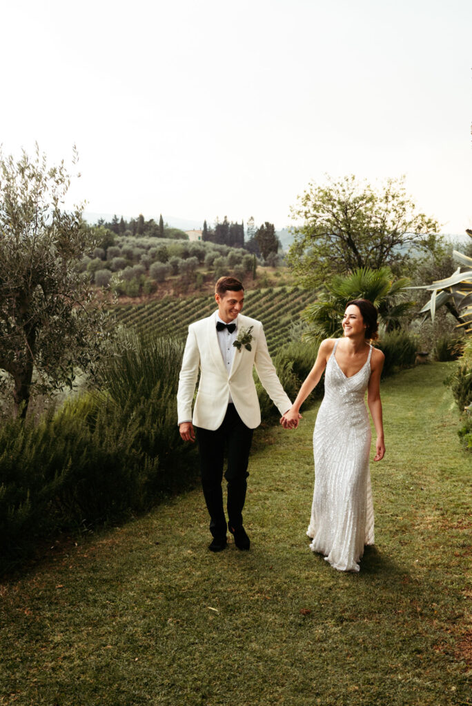 Bride and groom walk holding hand with Tuscany countryside on the background