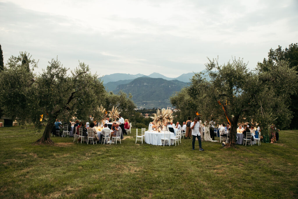 Outdoor wedding dinner setup with guests among olive trees in Salò, Lake Garda