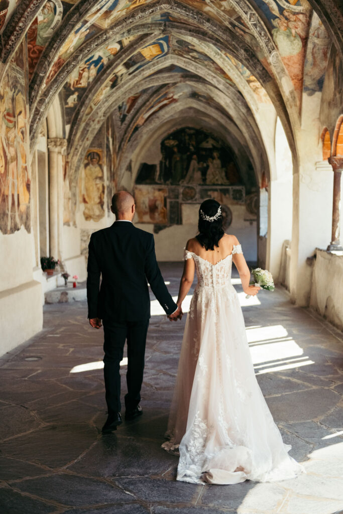 Intimate Italy Elopement in Dolomiti mountains, bride and groom walk down a decorated abbey