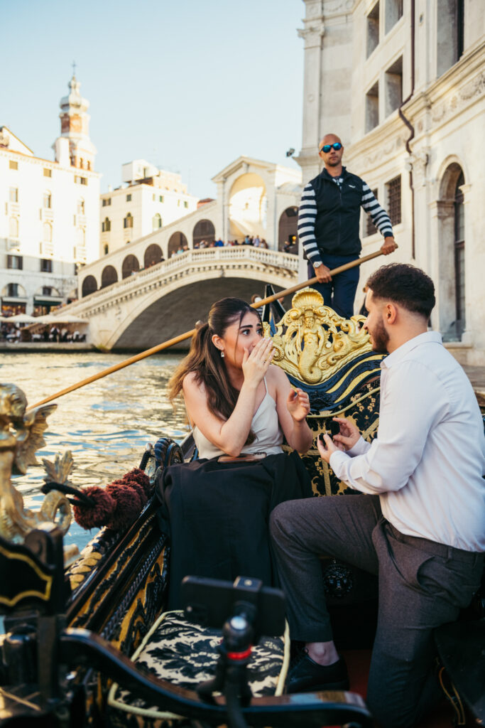 Man proposing to his partner on a gondola under the Rialto Bridge in Venice