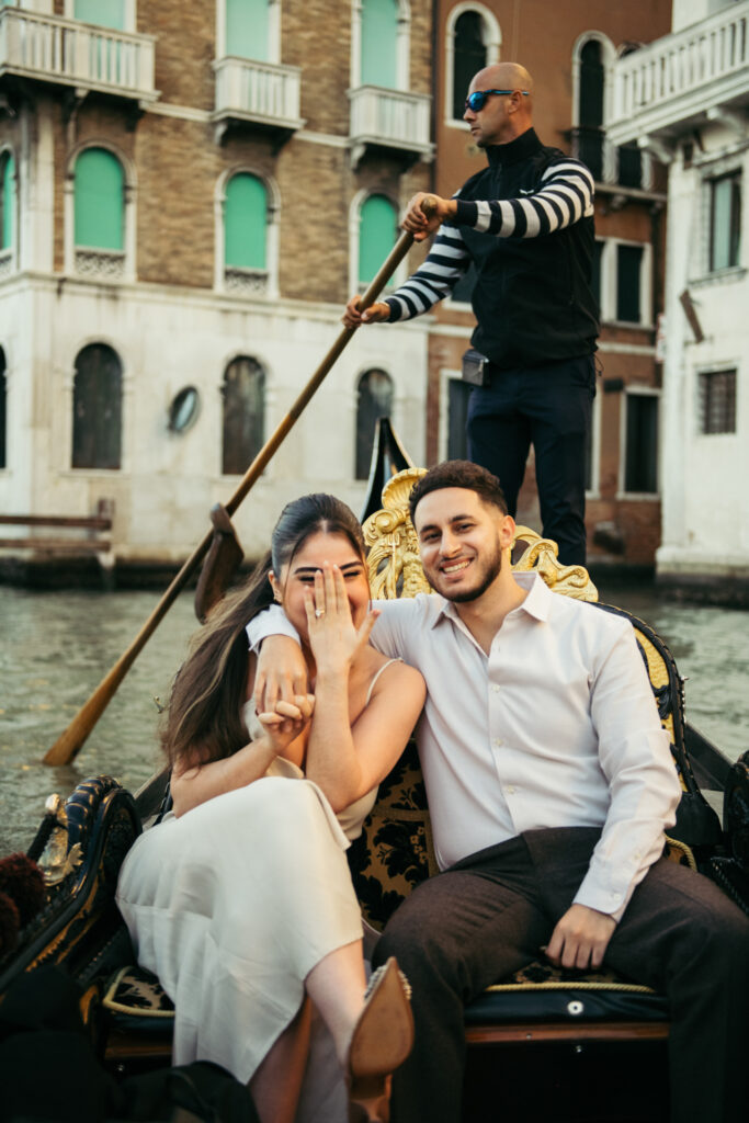 Happy couple on a gondola in Venice, showing off the engagement ring