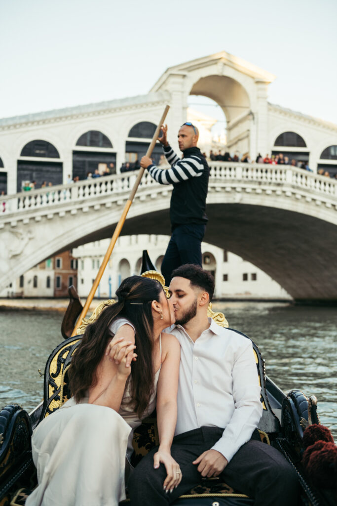 Boy and girl kissing on a gondola under the Rialto Bridge in Venice during a proposal photoshoot