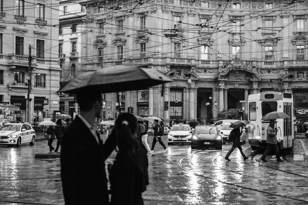 Black and white photo of couple looking at bustling Piazza Cordusio, Milan in the background