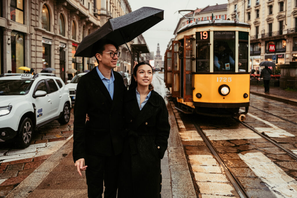 Couple walking with umbrella through Milan streets as a vintage tram passes by
