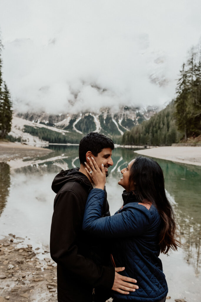 Couple smile at each other after getting engaged in Lake Braies, Italy