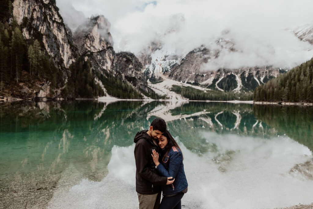 Couple hugs and closes eyes against the stunning backdrop of Lake Braies at Dolomites in Italy