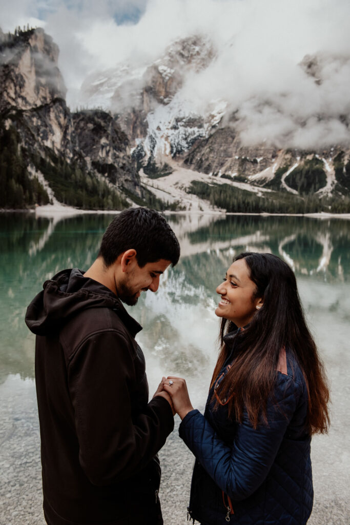 Couple holding hands and smiling at each other with Lake Braies on the background