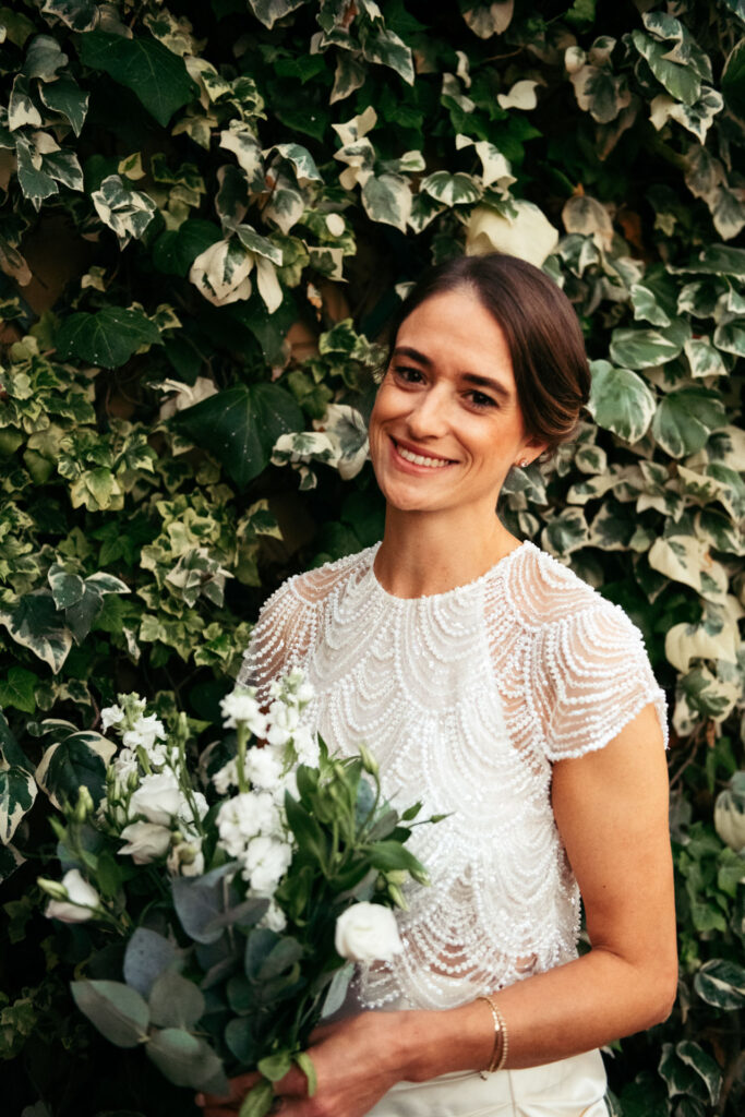 The bride in her wedding dress, smiling and looking in the camera while holding the bouquet