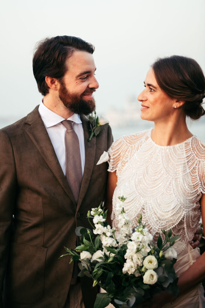 Bride and groom tenderly smiles at each other in a beautiful portrait