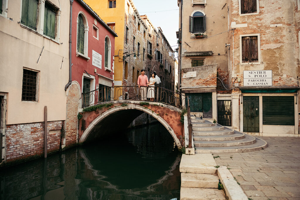 Bridge in Venice with colorful buildings and a couple standing on it