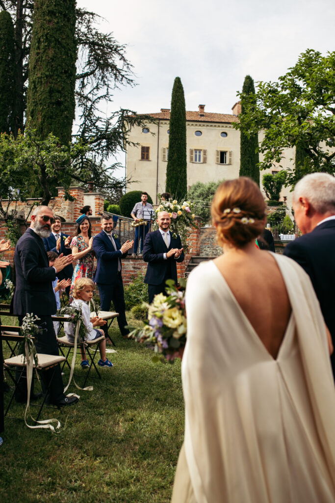 Bride and her dad walking down the aisle while the groom looks at her