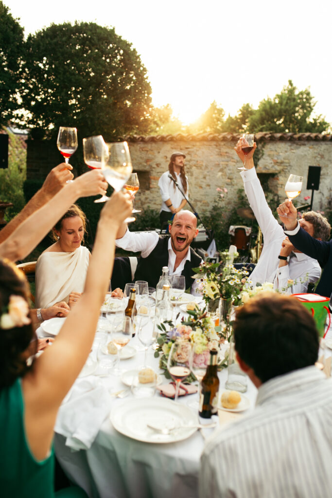 Bride, groom and friends celebrating and raising glasses at sunset during the wedding reception in the Langhe, Piedmont