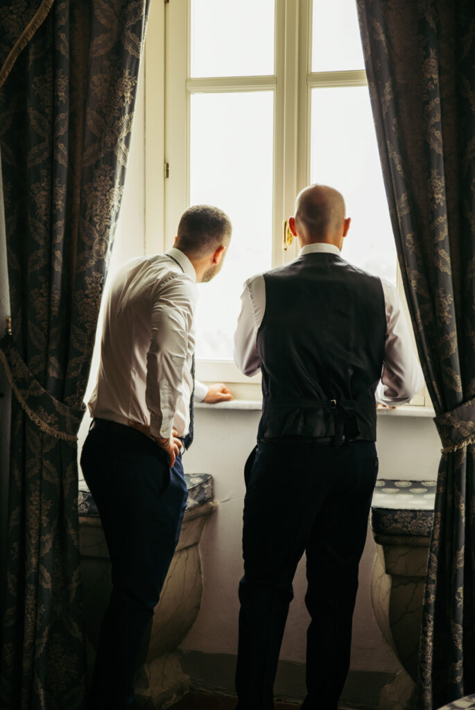 Groom and best man looking out of the window while getting ready