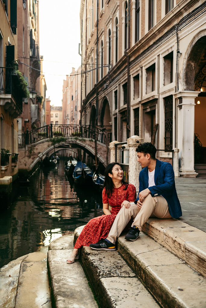 Couple sitting on the steps of a canal in Venice Italy while taking their engagement photoshoot