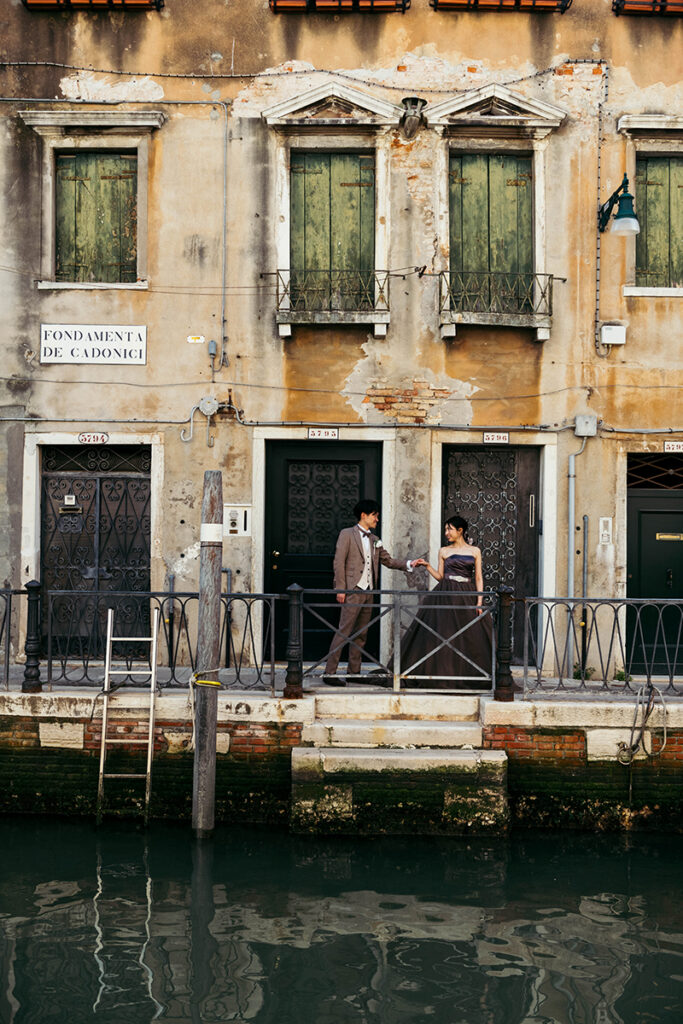 Japanese couple eloping in Venice, they pose on the other side of the canal wearing brown wedding dresses