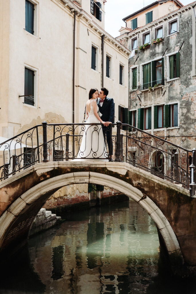 Couple standing on a stone bridge over a quiet canal during their romantic photoshoot — planning a Venice elopement with intimate moments away from the crowds.