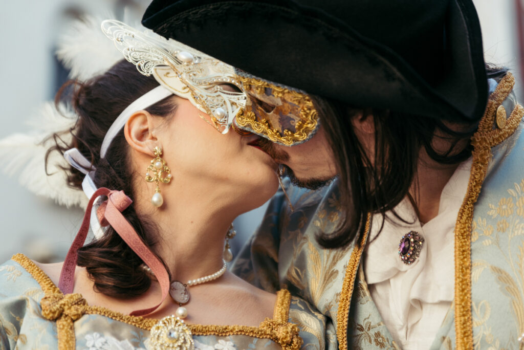 Close-up of a romantic kiss between a couple wearing ornate Venetian masks during Venice Carnival