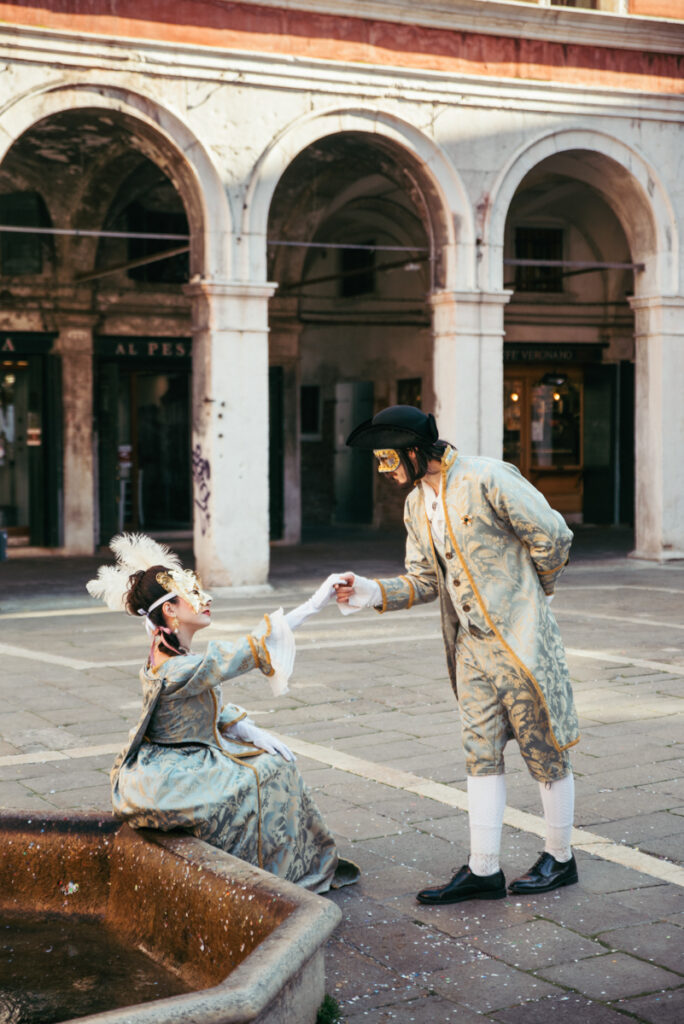 Venice Carnival couple in 18th-century costumes, as a gentleman elegantly holds his partner’s hand in a romantic gesture.