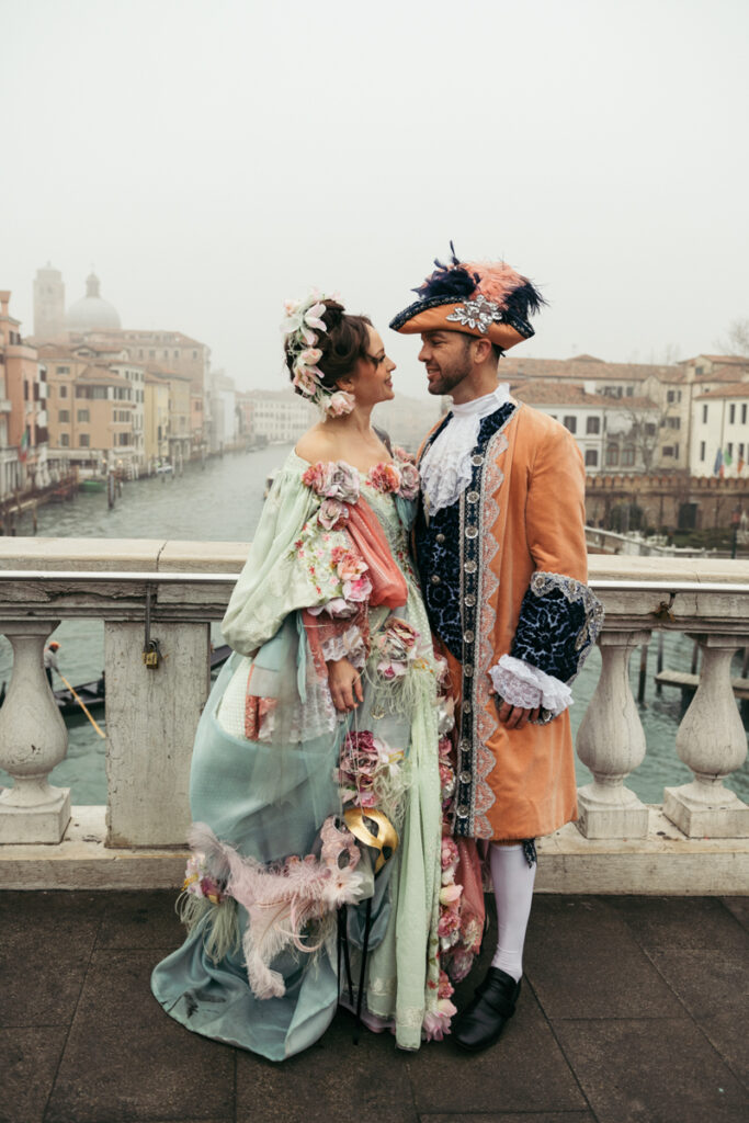 Venice Carnival couple in 18th-century costumes gazing at each other on the Ponte degli Scalzi in Venice