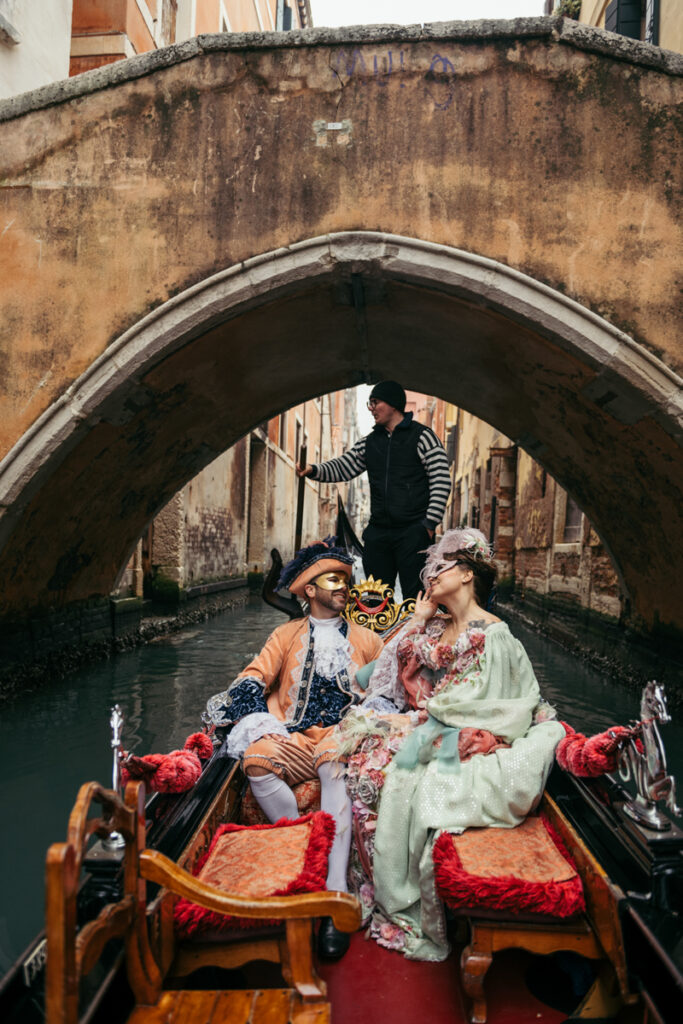 Couple in Venetian Carnival costumes captured in a gondola under a historic bridge