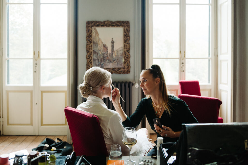 Bride smiling as her makeup artist applies the final touches, creating an intimate and relaxed pre-ceremony vibe.