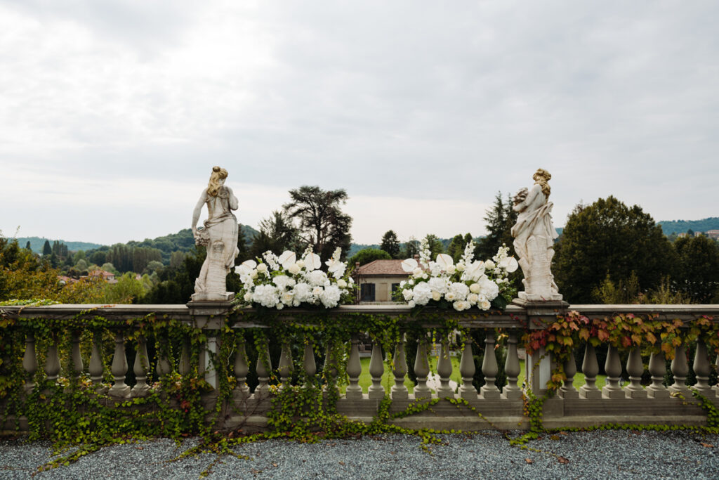 Close-up of the floral setup for an outdoor elopement ceremony in Italy, with elegant statues in the background.