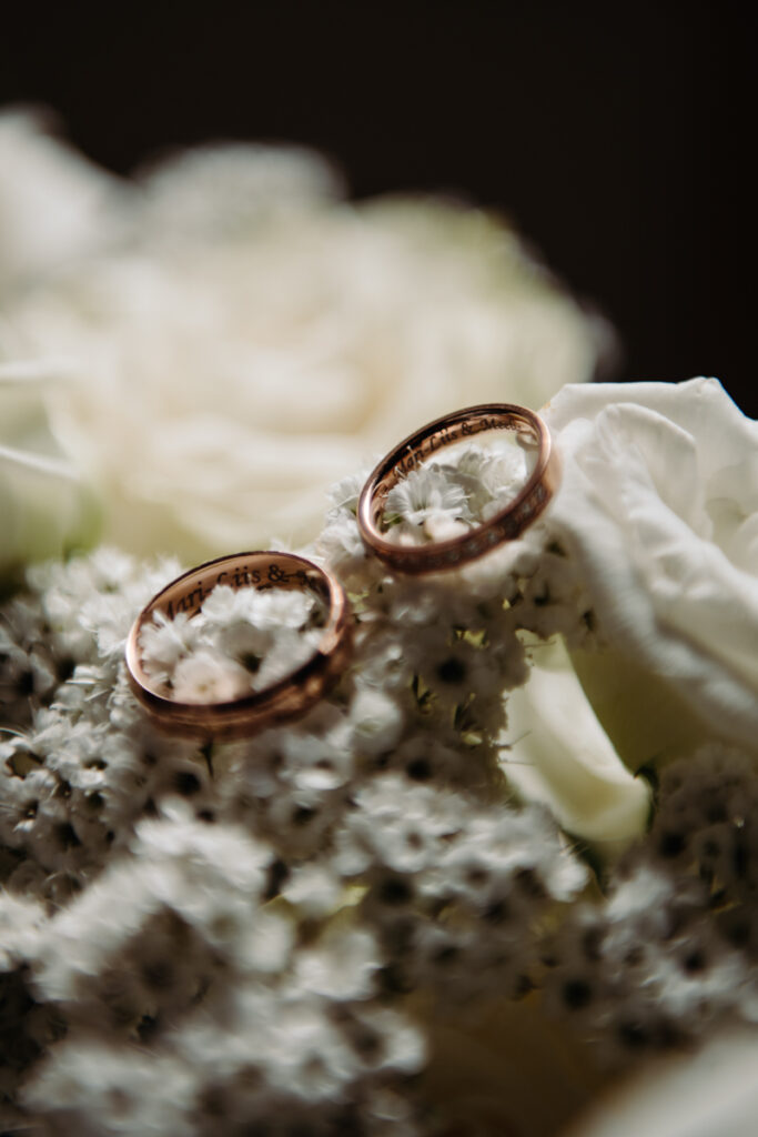 Detail shot of two wedding rings resting on baby’s breath flowers, with white roses in the background.