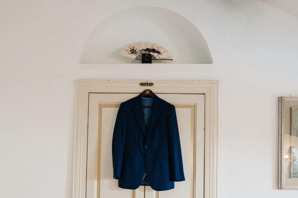 Groom’s blue suit jacket hanging on a door, framed by classic white architecture.