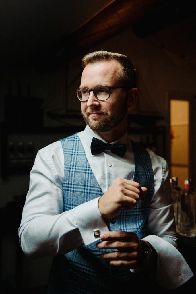 Groom adjusting his cufflinks, wearing a plaid vest and bow tie, getting ready for the ceremony.