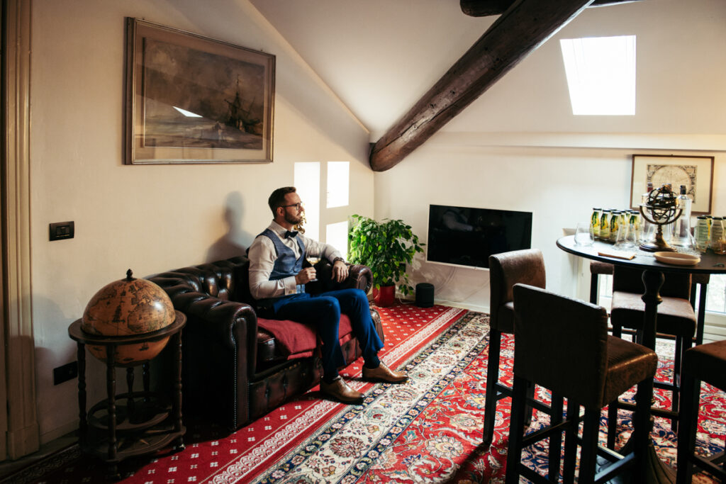 Candid moment of the groom relaxing while waiting in a vintage-style living room.