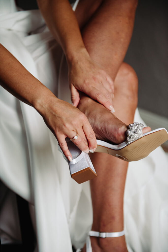 Bride adjusting her elegant white heels, captured in a candid, intimate moment during the getting ready.