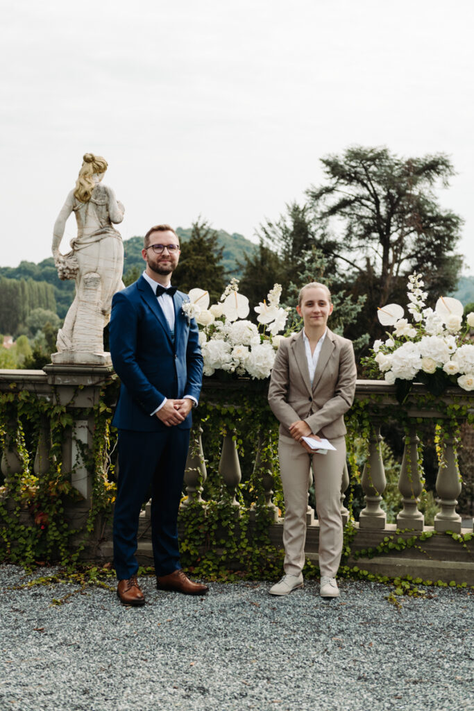 Groom standing with the celebrant, both smiling in front of an elegant floral backdrop.