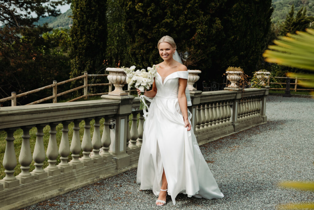 Bride walking gracefully along a stone path, holding her dress lightly with one hand.