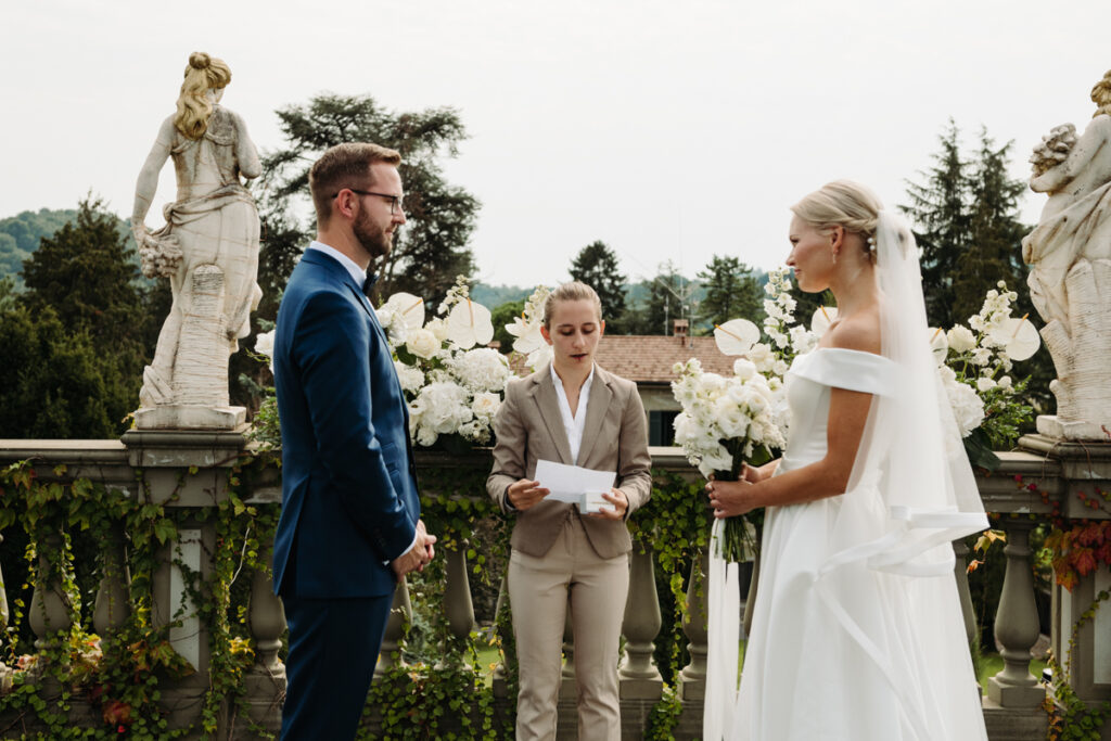 The couple standing together as the celebrant reads, framed by elegant floral arrangements.