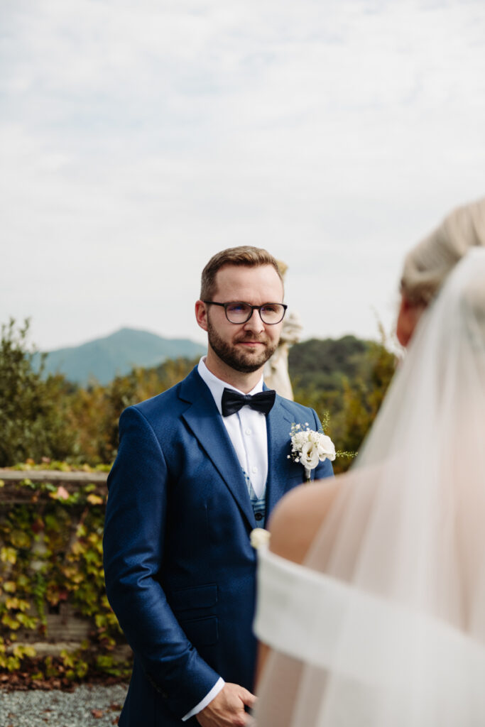 Groom looking at the bride with a soft smile, with a scenic Italian landscape behind him.