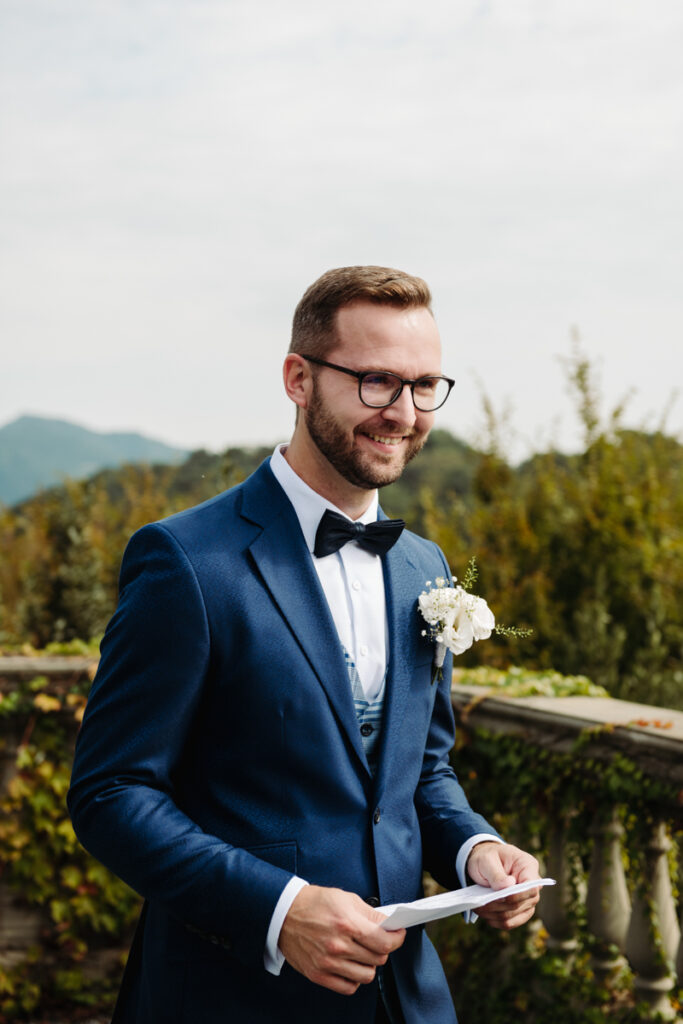 Groom laughing softly during the ceremony, surrounded by the greenery and elegant details of the venue.