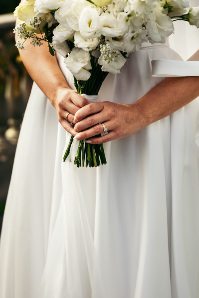 Detail shot of the bride holding her white bouquet with both hands, her wedding dress elegantly flowing.