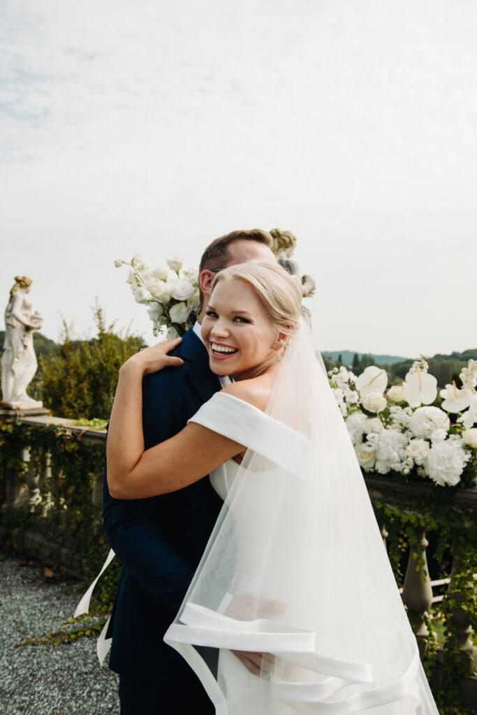 Loving embrace between the smiling couple, surrounded by white floral decorations.