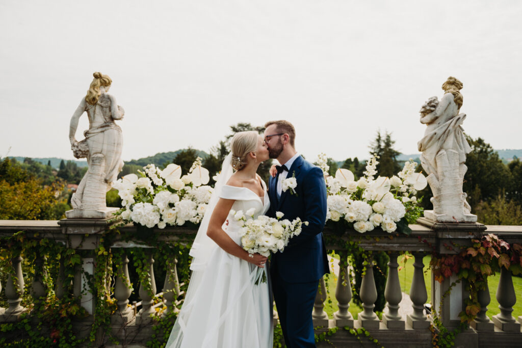 Romantic kiss between the bride and groom during their symbolic ceremony, with white flowers in the background