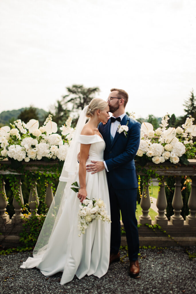 The couple standing in front of an elegant floral arrangement, holding hands and sharing a tender glance